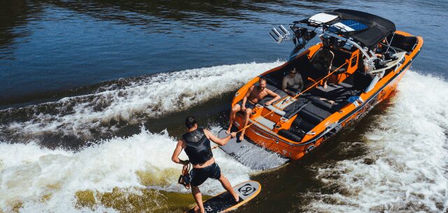 A person wakeboarding behind an orange boat on a sunny day.