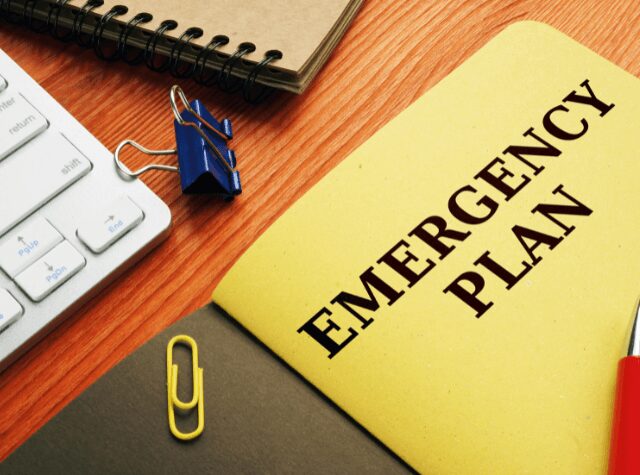 An emergency plan document with office supplies on a wooden desk.