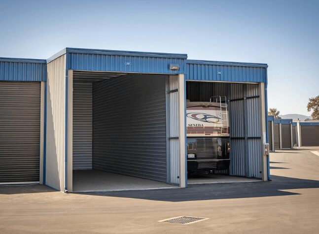 A blue metal garage with a partially open door revealing an RV inside.